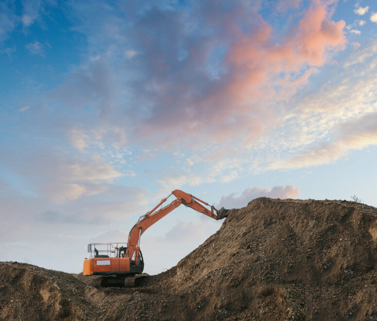 Excavator bulldozer in sandpit with raised bucket over blue cloudscape sky.