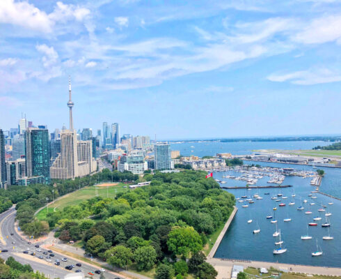 Skyline of Toronto with the CN Tower and skyscrapers. In the foreground, a green park and marina with sailboats.