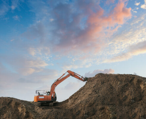 Excavator bulldozer in sandpit with raised bucket over blue cloudscape sky.